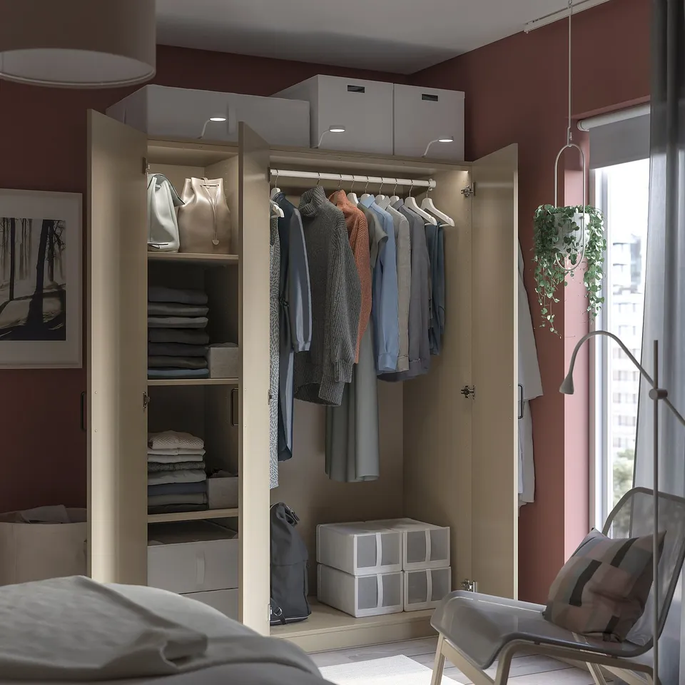 Open wardrobe with grey, white, and beige clothes and storage boxes, lit top shelves, modern chair near window.