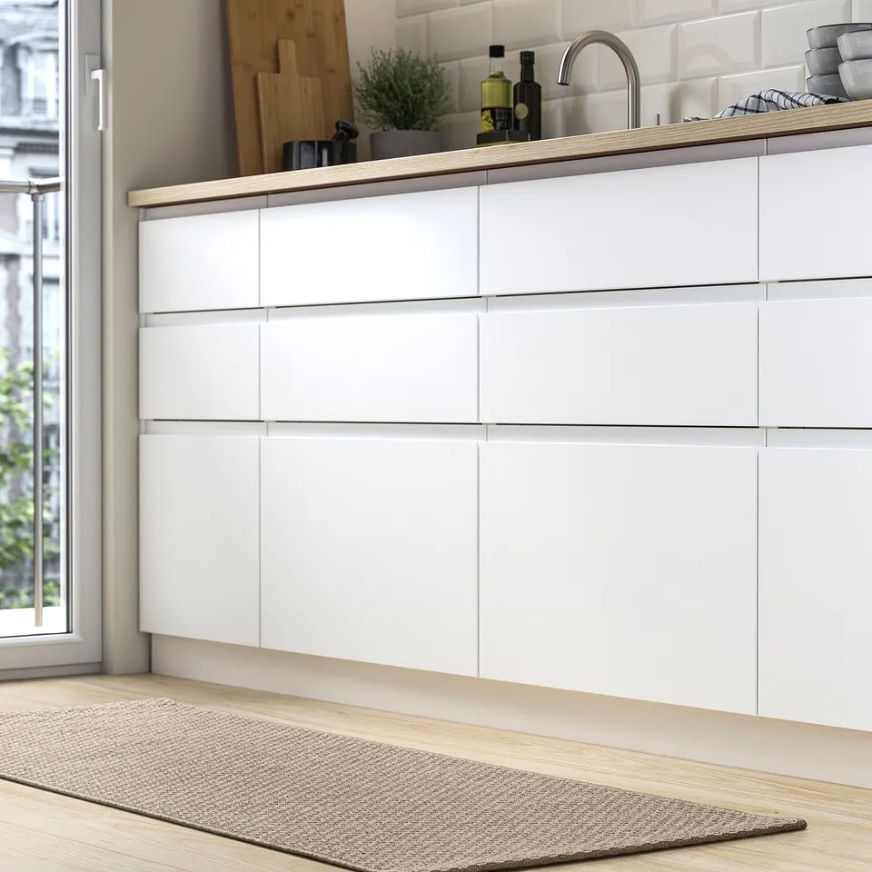 A modern kitchen with a white cabinet, wooden floor, and MORUM rug in neutral tones, providing a cosy atmosphere, placed in front of the sink.