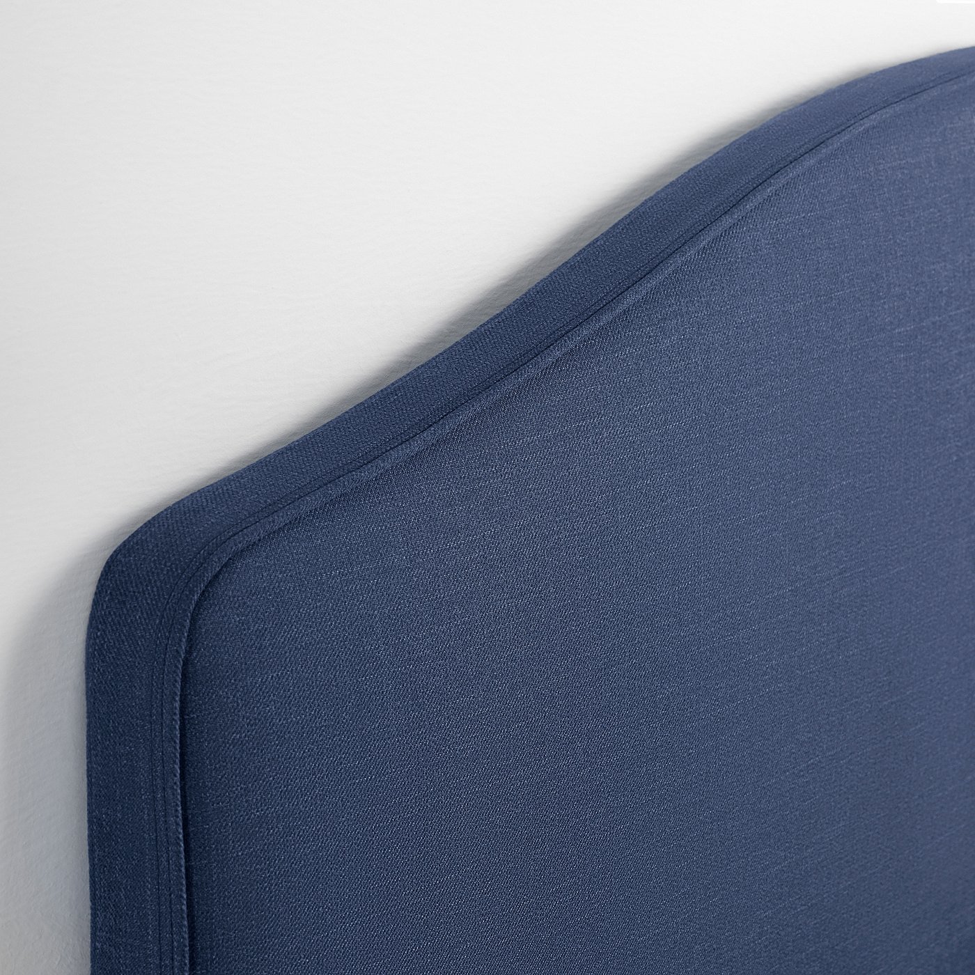 Close-up of navy-blue bed frames upholstered headboard with neat piping and smooth fabric.