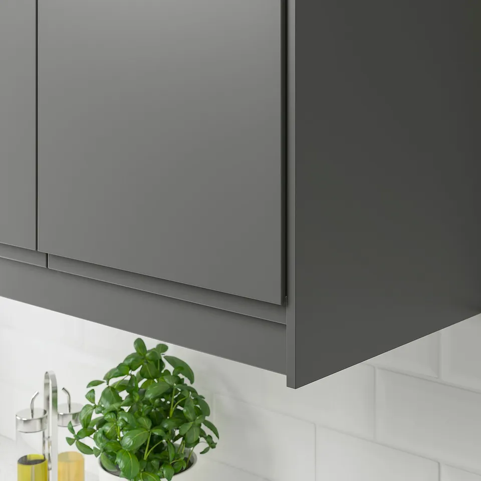 Dark grey kitchen cabinet trim hides lighting and cords. Greenery and small bottles below.