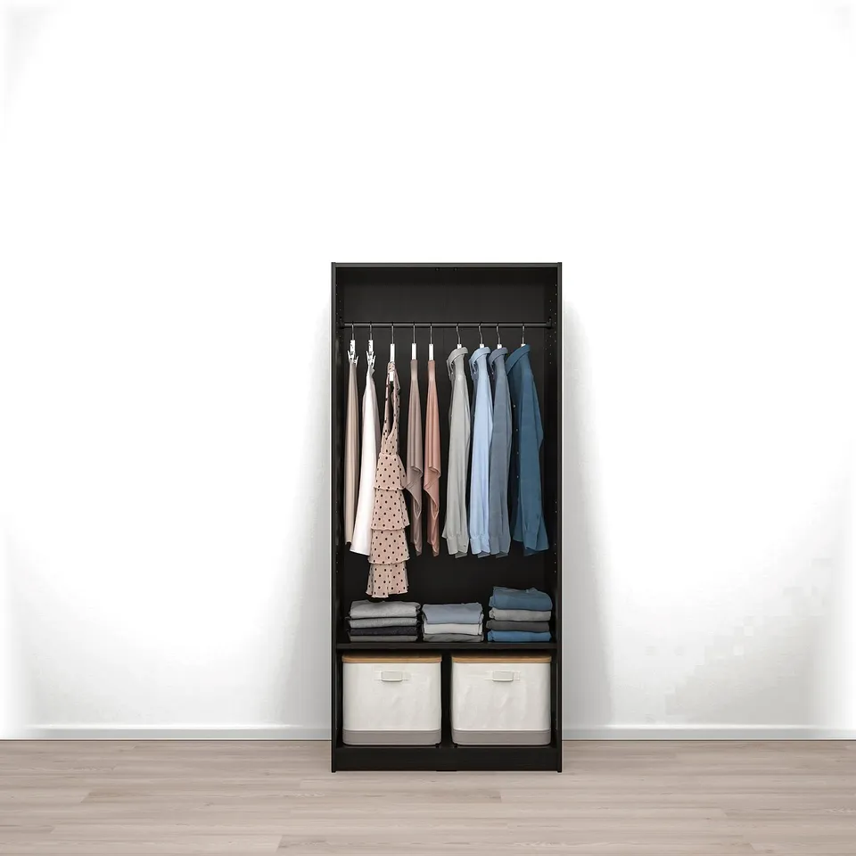 Black wardrobe with hangers for clothes and bins for storage, against a white wall.