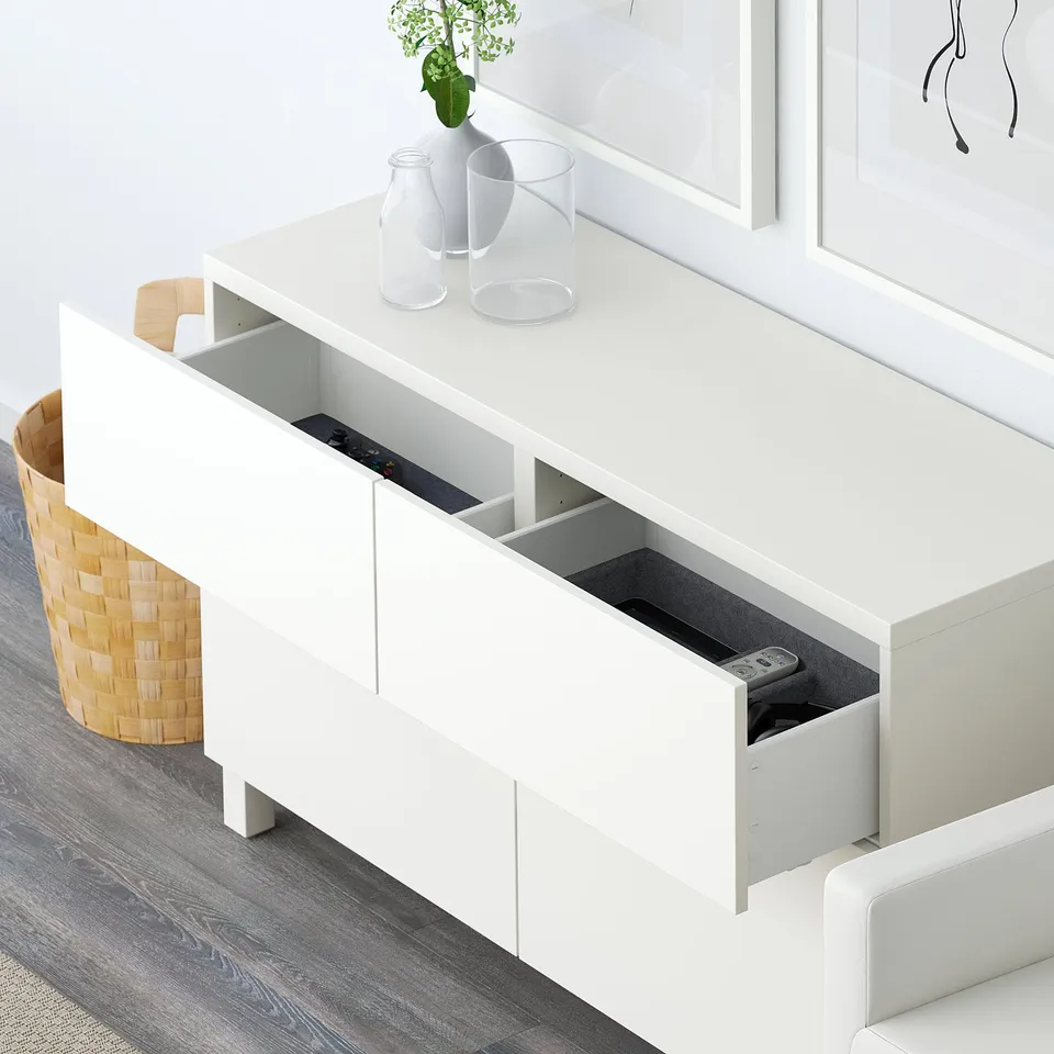 White sideboard with drawers and open storage. Remote on drawer, décor on top.