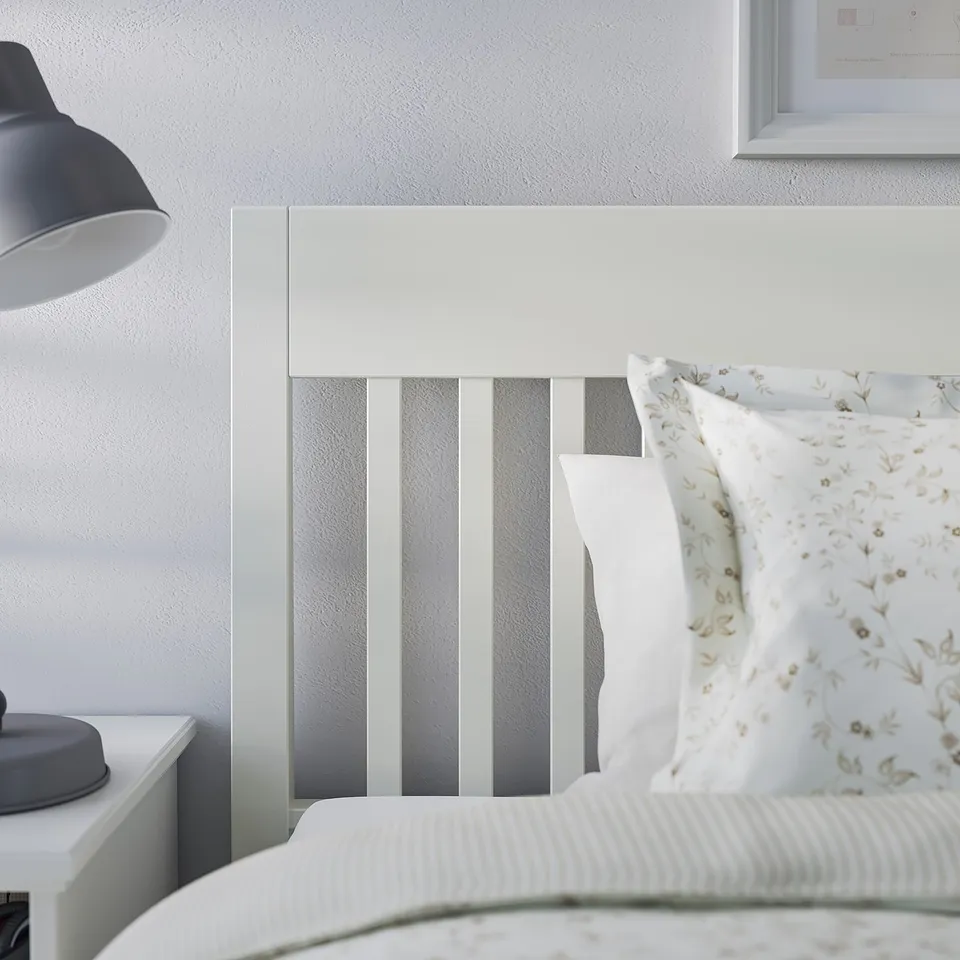 Cosy bedroom with white IDANÄS bed featuring striped headboard and floral pillow on comfy linens. Blue lamp beside.