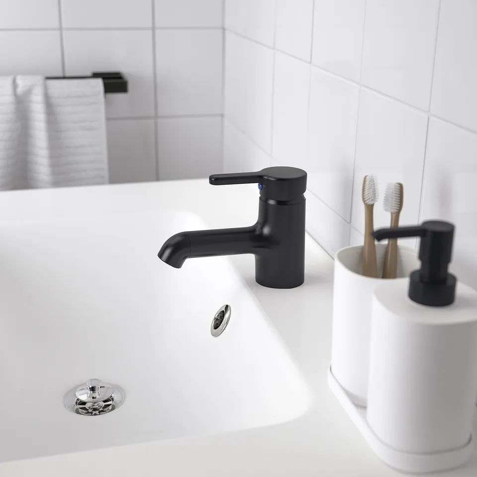 Modern bathroom sink with matte black SALJEN tap, smaller than toothbrush holder, set against white tile backdrop.