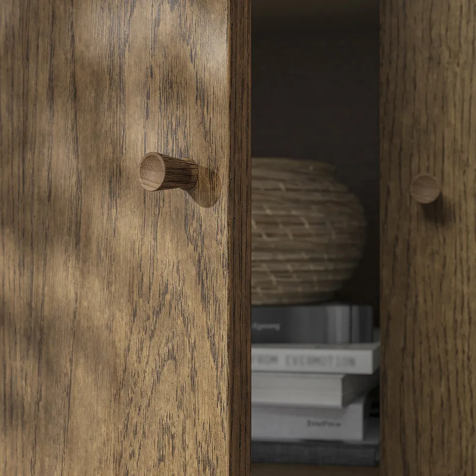 Wooden cabinet with visible grain and cylindrical knobs, partially open revealing shelves with items.