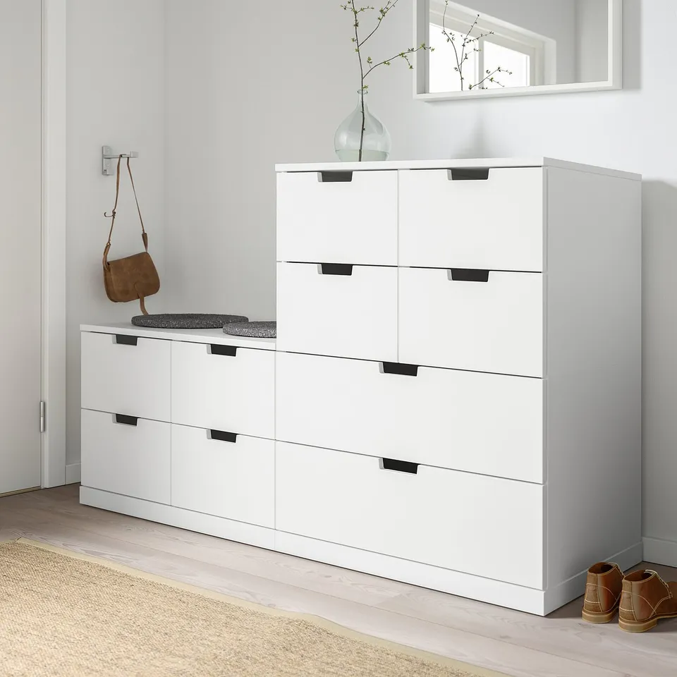 Modern white NORDLI chest in entryway. Wide, low size with drawer handles. Placed under a wall shelf, fits large entryway.