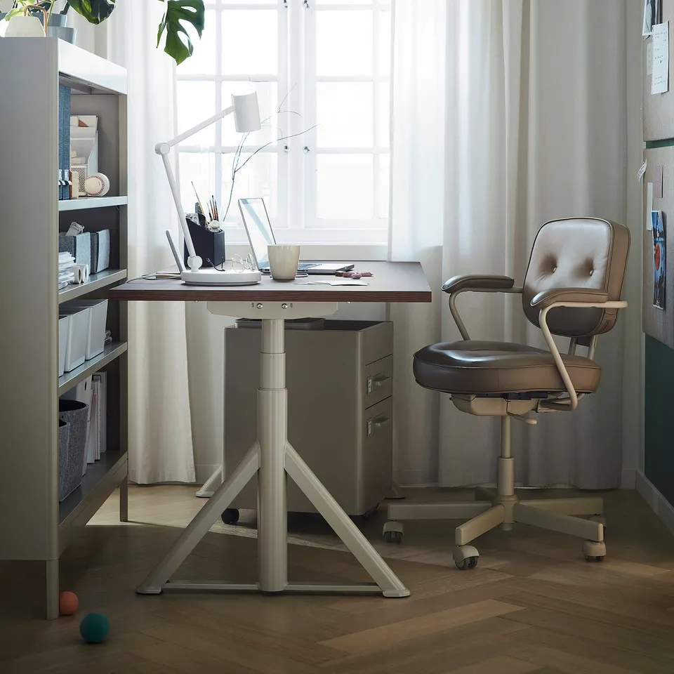 Modern home office with IDÅSEN desk, grey chair, and bookshelf. Wood floor, natural light, plants, and decor.
