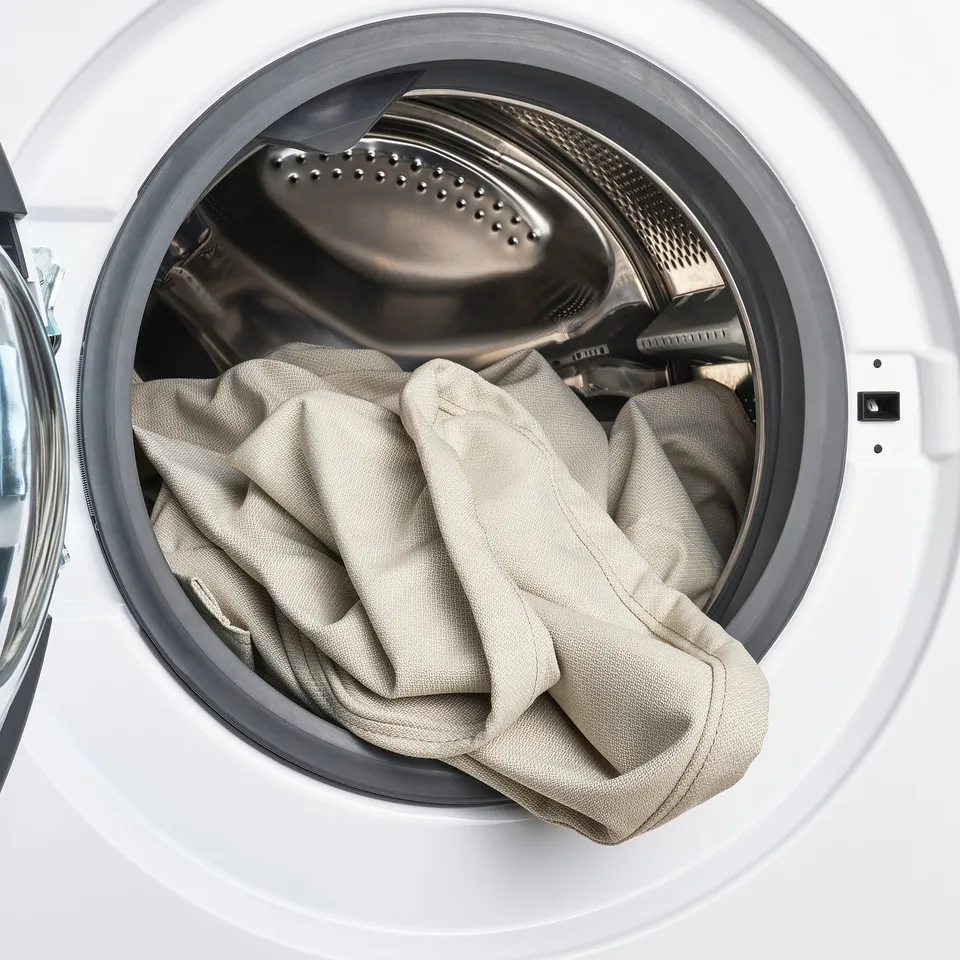 White washing machine with open door, containing rumpled beige fabric.