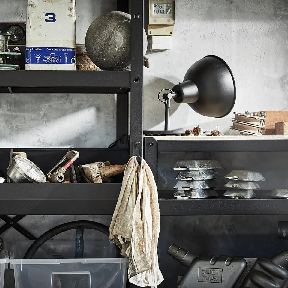 Black metal shelf unit with various items stored. Includes tools, a lamp, and clear plastic bins. Industrial design.