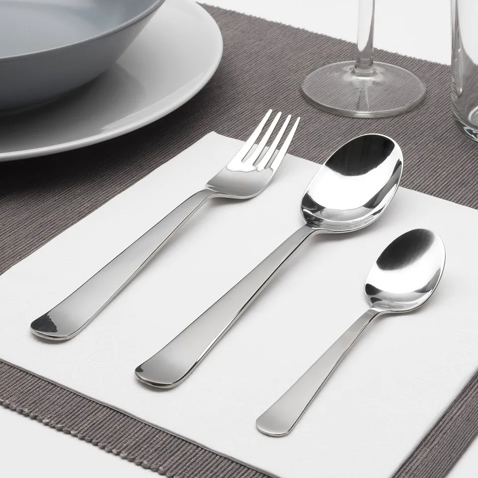 Polished metallic fork, spoon, and teaspoon neatly arranged on a white napkin, part of DRAGON cutlery set, suitable for elegant place settings.