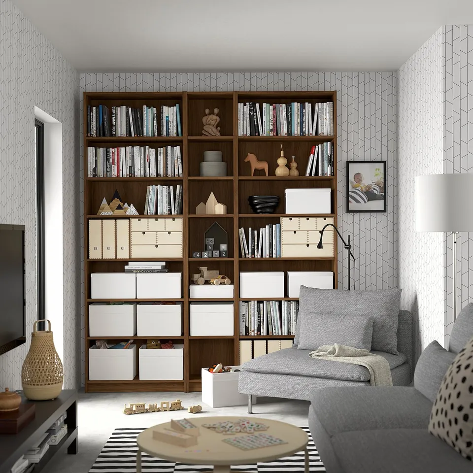 Wooden BILLY bookcase with books & decor, near grey sofa, puzzles on round table.