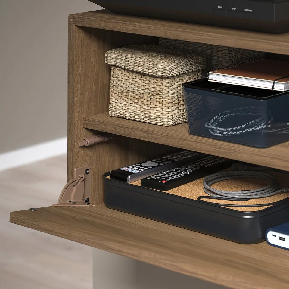 Wooden media storage unit with flip-open shelf, holding remote controls and cables.