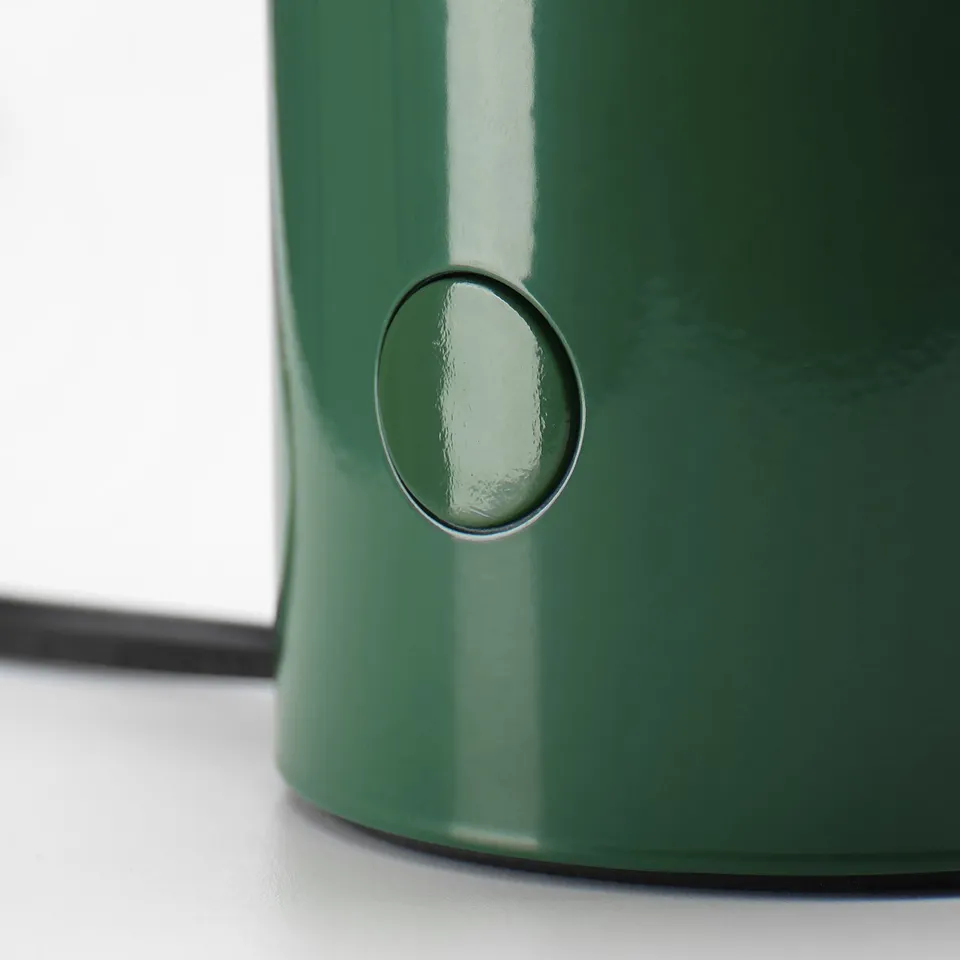 Green table lamp with sleek design, round button on side, shiny surface.