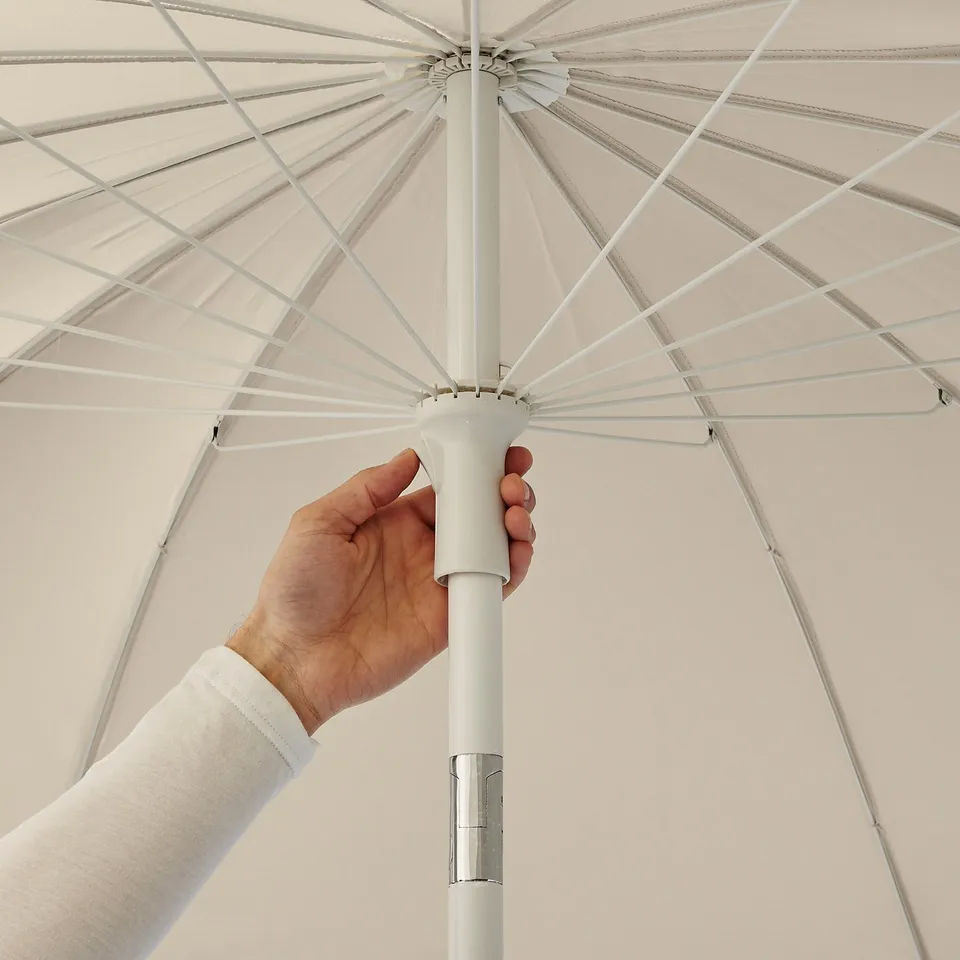 Hand holding adjustable parasol handle, tilting shade for comfort.