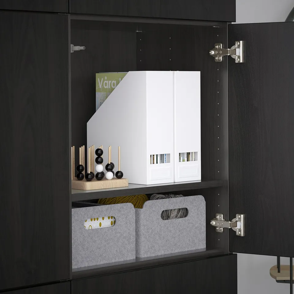 Black BESTÅ cabinet with adjustable shelves and hinges; white box and felt bins on top shelf, small decor items on middle shelf.
