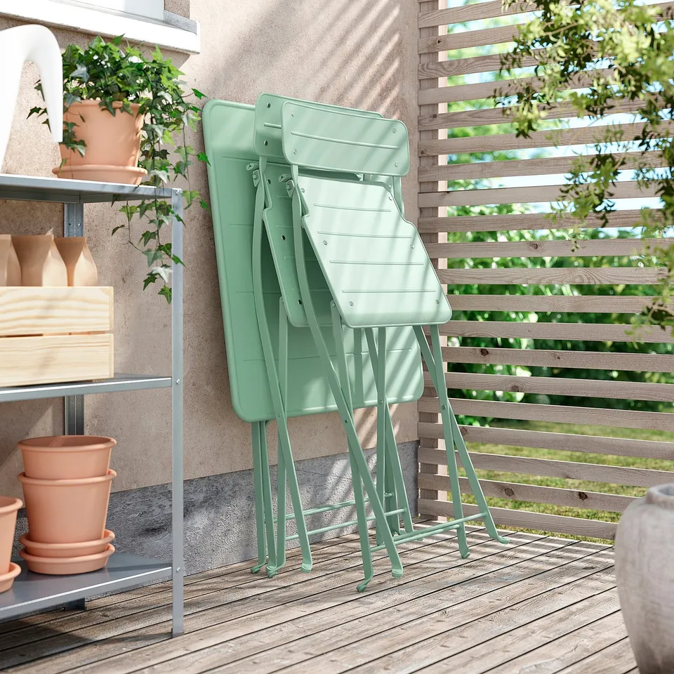 Outdoor space with folded green metal chairs, pots, and wooden fence.
