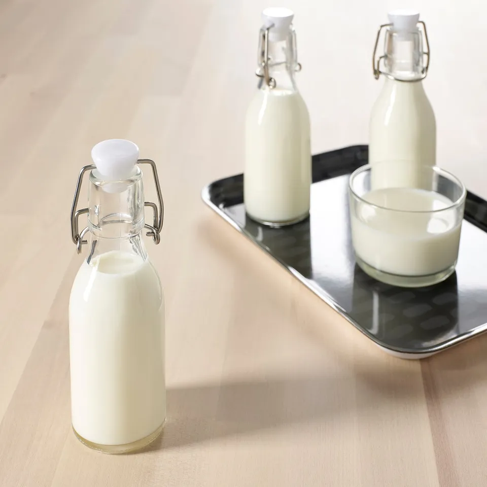 Three glass bottles with white stoppers on a wooden table; one bottle and a cup on a metal tray.