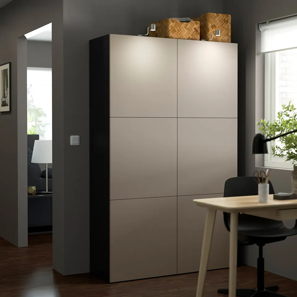 A modern BESTÅ storage unit in beige with four doors, two baskets, and a lamp.