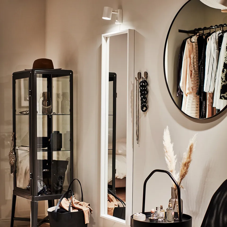 Modern room with black LINDBYN round mirror, sleek cabinet, and chair, displaying decor and clothes.