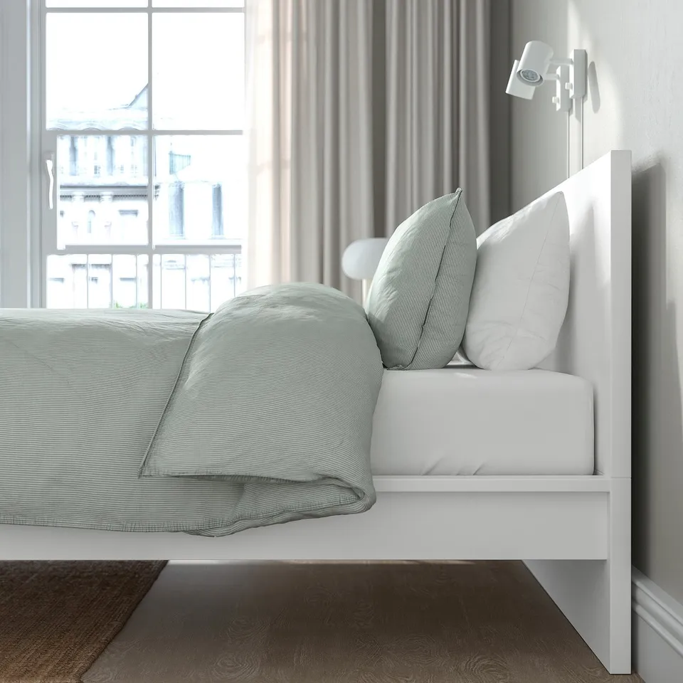Modern bedroom with MALM bed, green bedding, wall light, and window view.