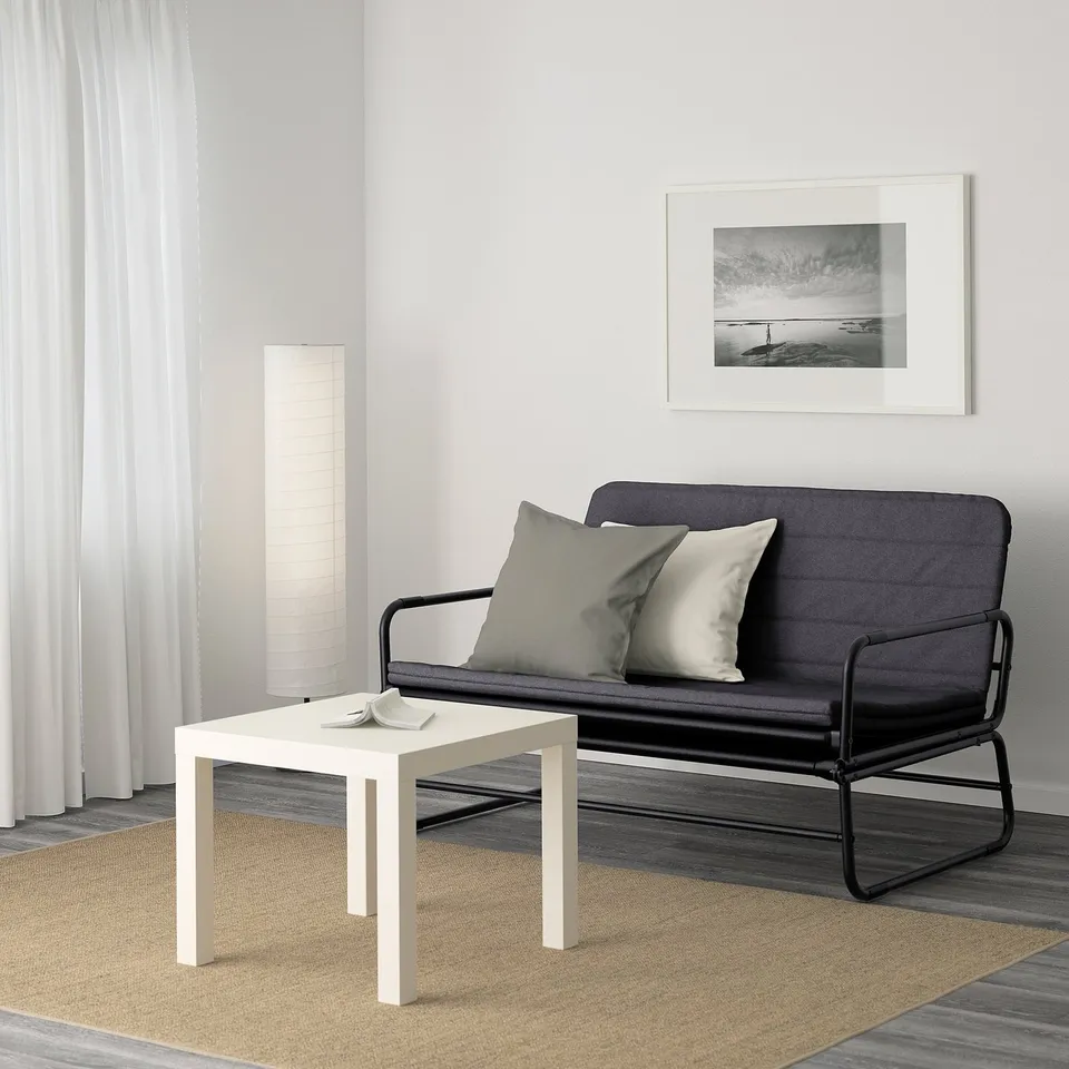 Minimalist living area with black sofa bed, white side table, and coastal photo.