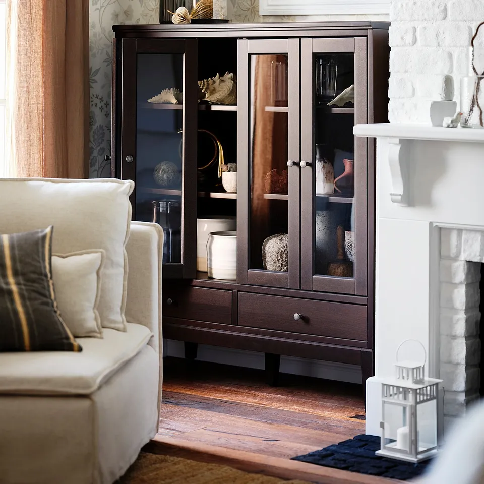 Elegant room with IDANÄS dark wooden display cabinet, glass doors, white sofa, patterned wallpaper, and fireplace.