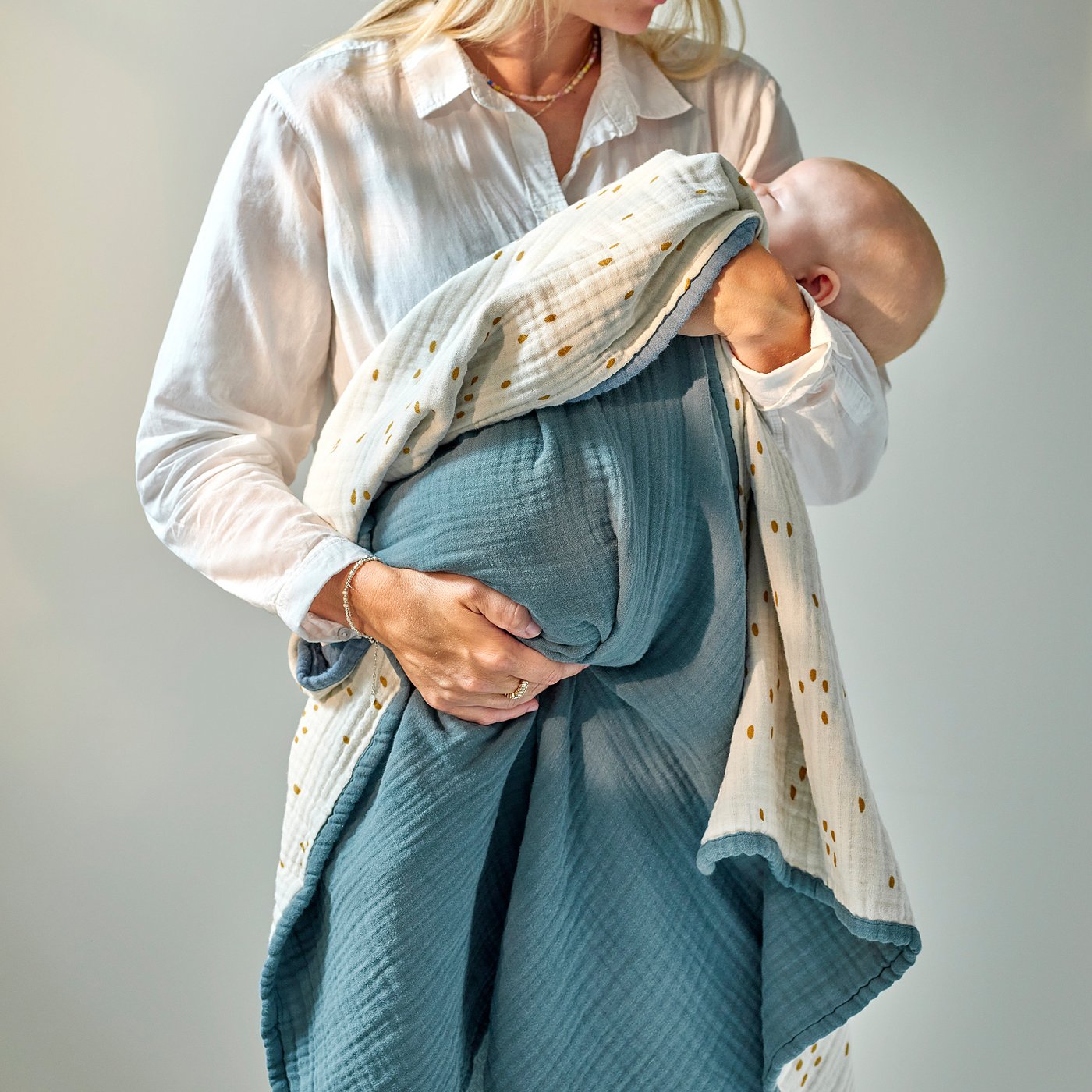 A person cradles a baby with a soft, blue and white muslin blanket, offering comfort and warmth.