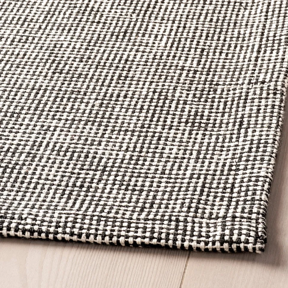 Black and white woven rug on wooden floor. Textured, high-quality cotton.