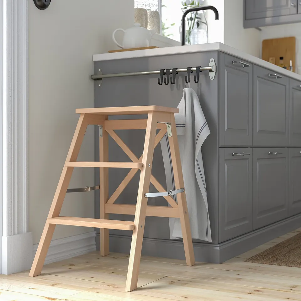 Natural beech BEKVÄM step stool, foldable, next to kitchen cabinets.