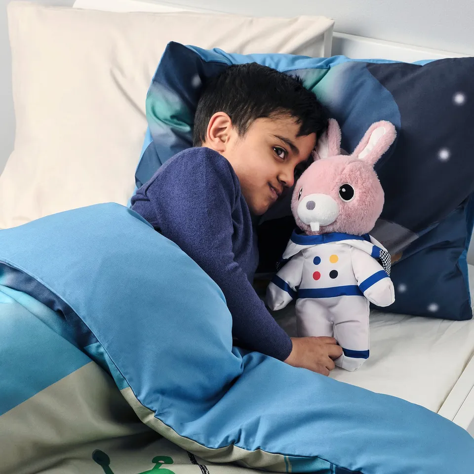 Boy in bed hugging soft astronaut rabbit toy; comfort and imaginative play.