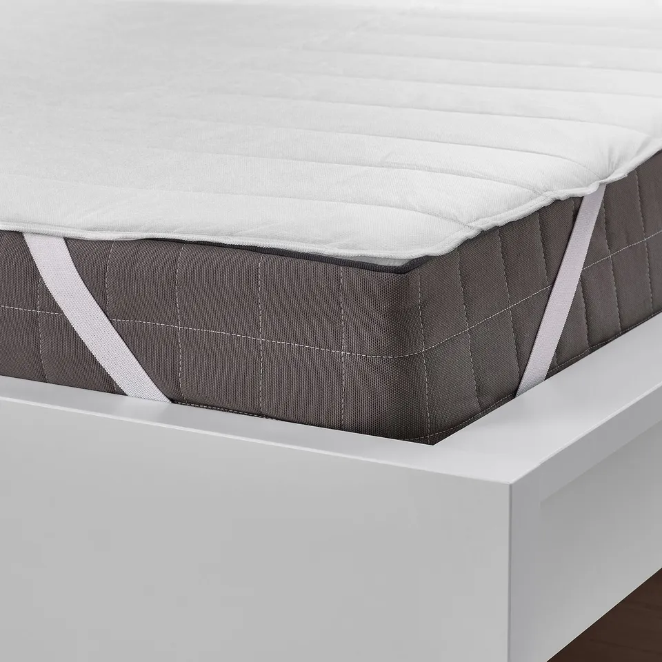 Mattress protector on white bed, elastic straps ensure it stays in place, protects from stains.