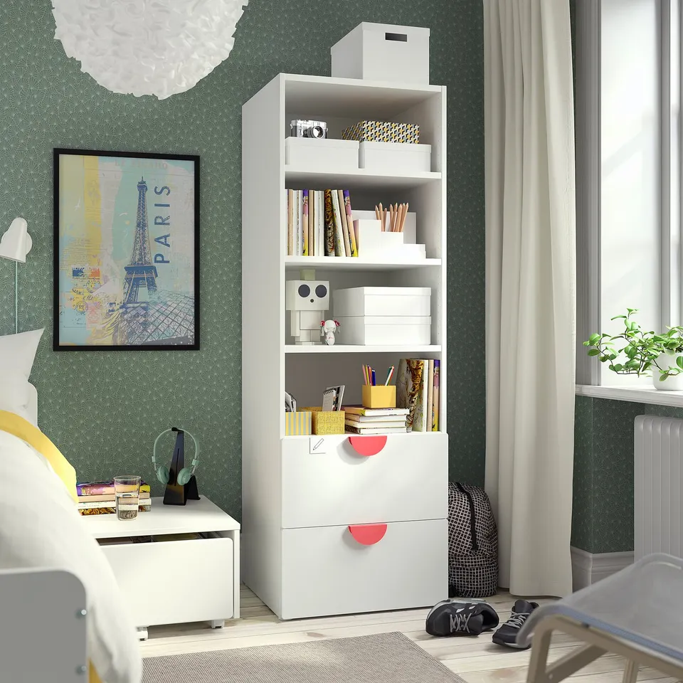 White bookcase in bedroom, filled with books, near window with curtains.