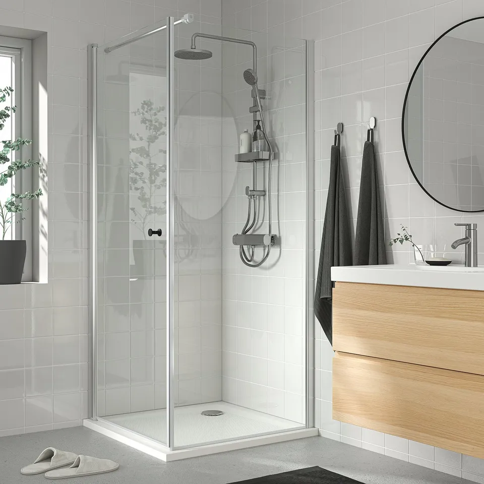 Modern bathroom with BROGRUND shower, glass door, mirror, vanity, towels, slippers.