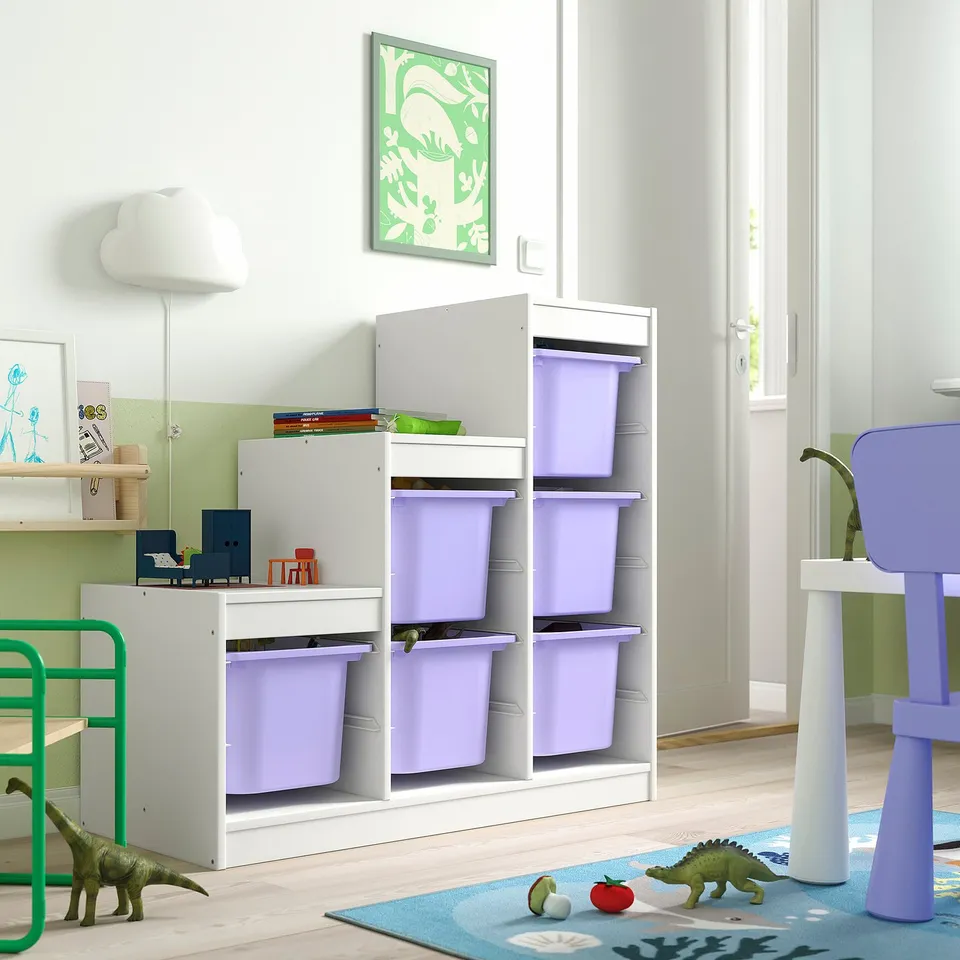 Childrens room with TROFAST storage, purple bins, dinosaurs, blue rug, green chair, wall lamp, artwork.