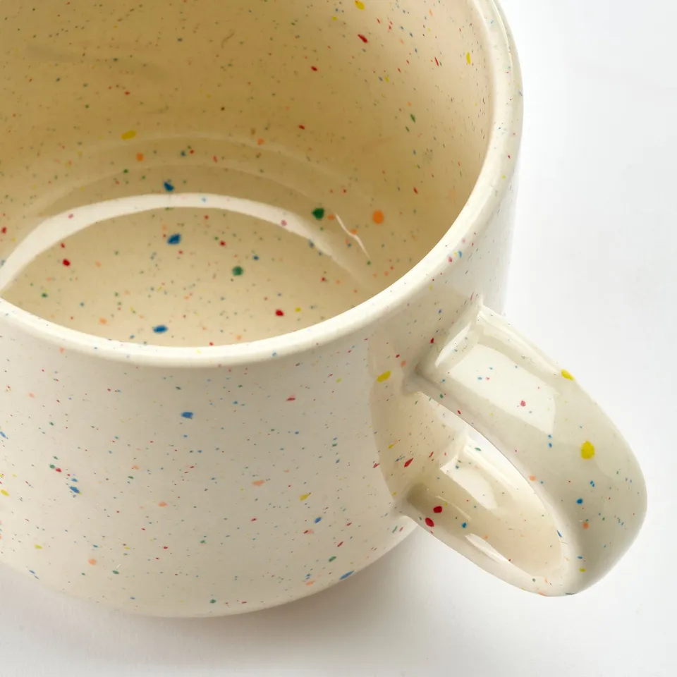 Handcrafted mug with multicoloured speckles, smooth handle, well-glazed surface, simple design.