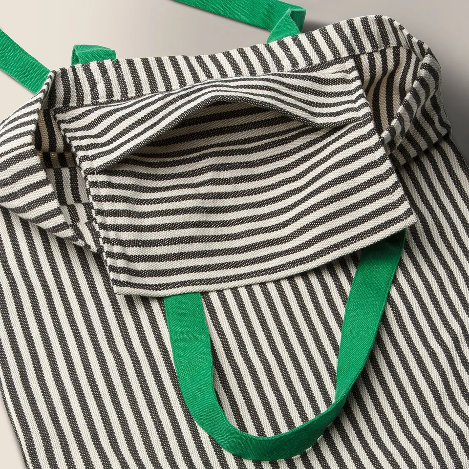 Striped tote bag with green handles, open top revealing inner pocket. Eco-friendly, handwoven cotton design.