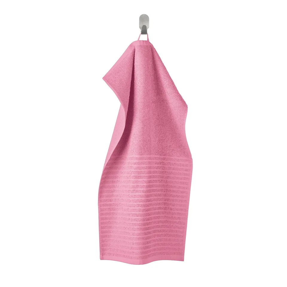 A bright pink VÅGSJÖN towel hangs neatly on a hook, featuring a soft, ribbed cotton design for absorbance and quick drying.