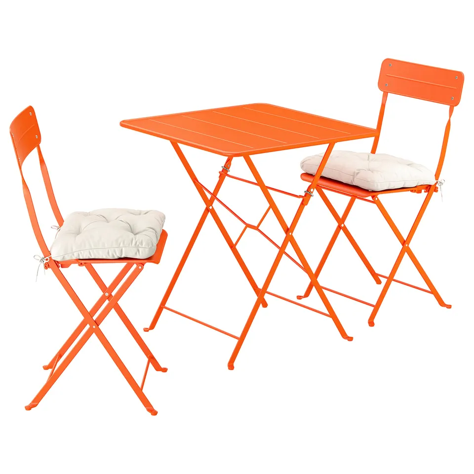 Bright orange metal balcony set with two folding chairs and a square table, cream cushions.