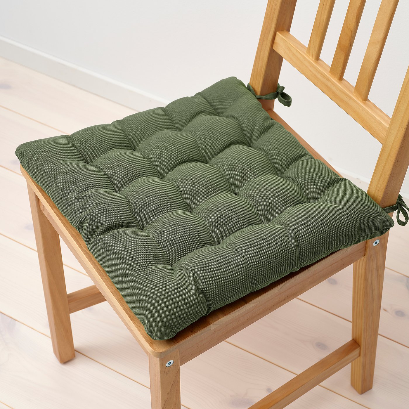 Green tufted chair pad on wooden chair. Thick, cushioned, with ties to secure.