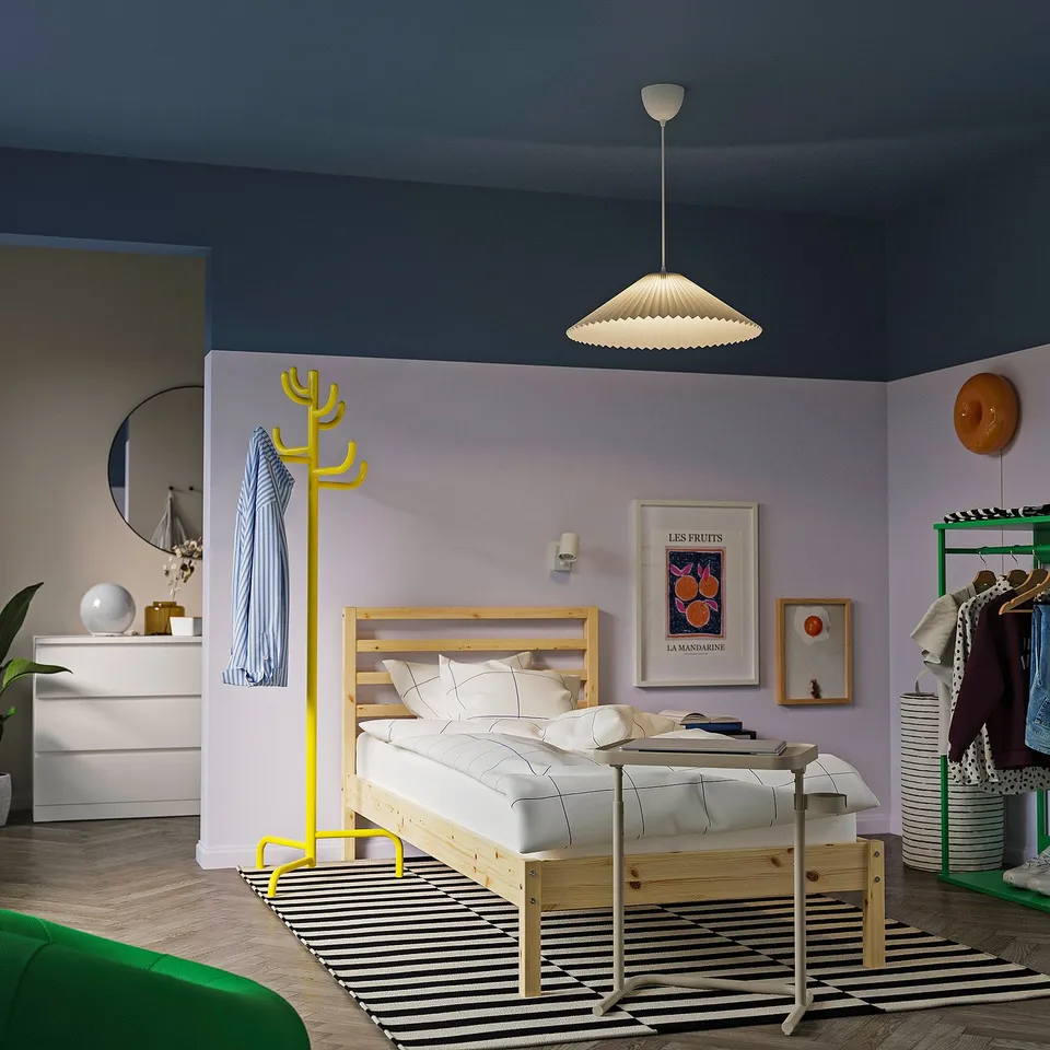 Bedroom with blue-purple walls, white KUDDLAVA light, yellow coat rack, wooden bed with white linens.