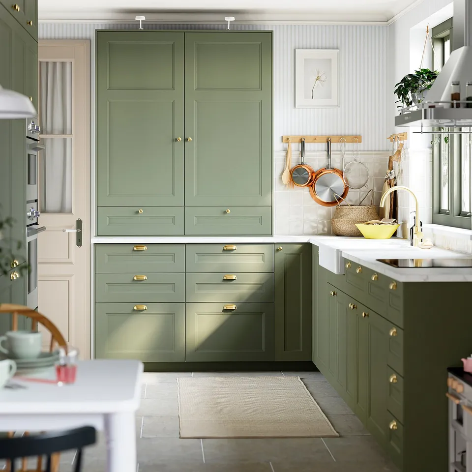 Organised kitchen with green cabinets, brass hardware, white counters, hanging utensils, and ENERYDA knobs.