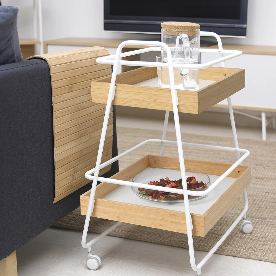 White bamboo trolley with 2 shelves, snacks, and jars, next to blue couch.
