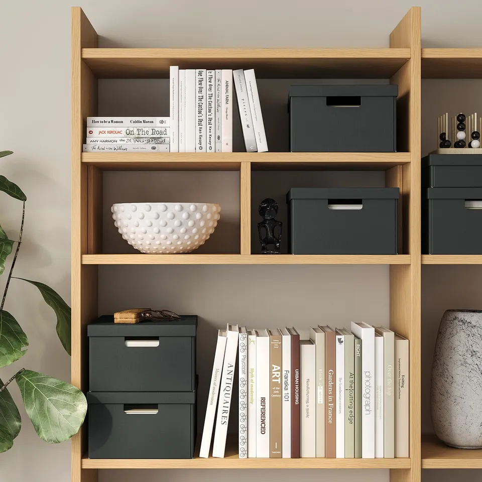 Wooden bookshelf with books, grey storage boxes, white bowl, and small sculpture.