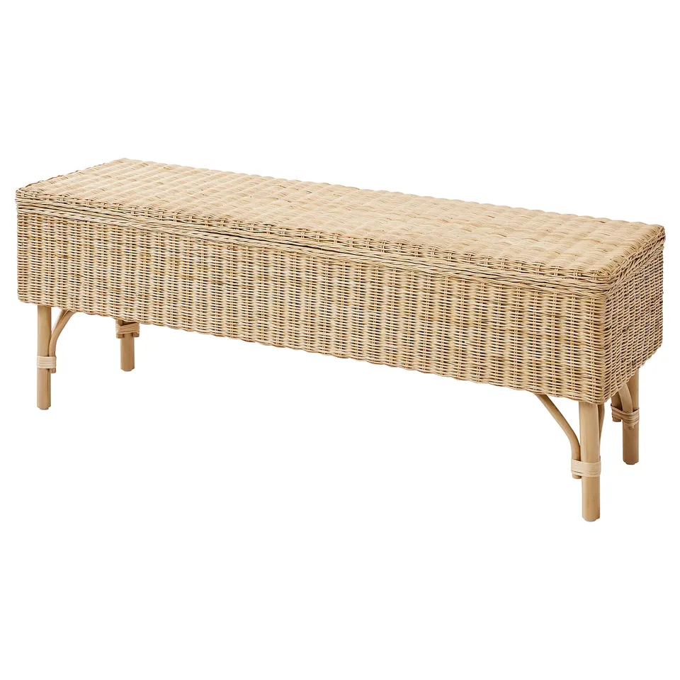 The TOLKNING bench is a natural rattan storage seat with bamboo legs. Its beige, rectangular, and finely woven, offering both seating and storage.