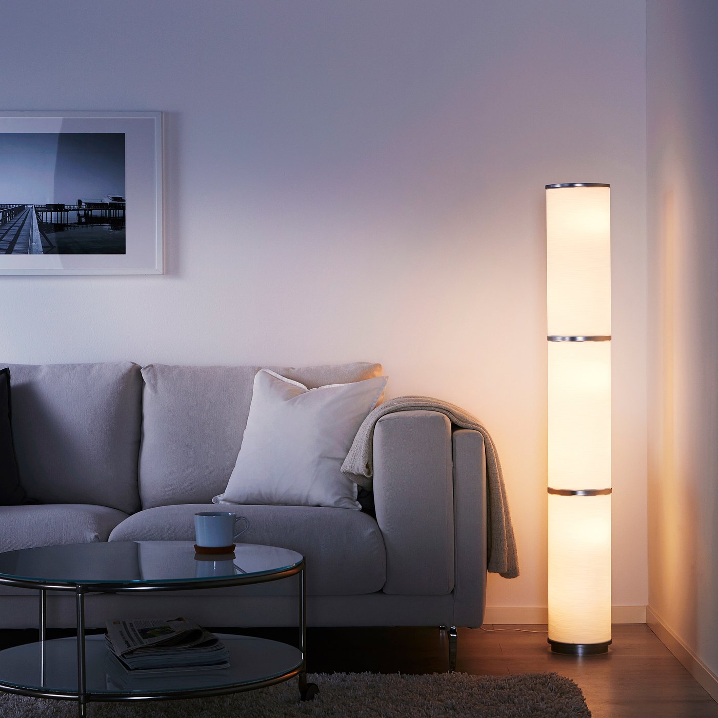 Modern living room with grey sofa, soft VIDJA lamp light, and framed photo.
