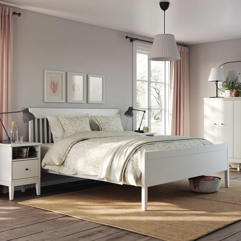 Modern bedroom with IDANÄS white bed, soft linens, nightstands, lamp, rug, and botanical prints.