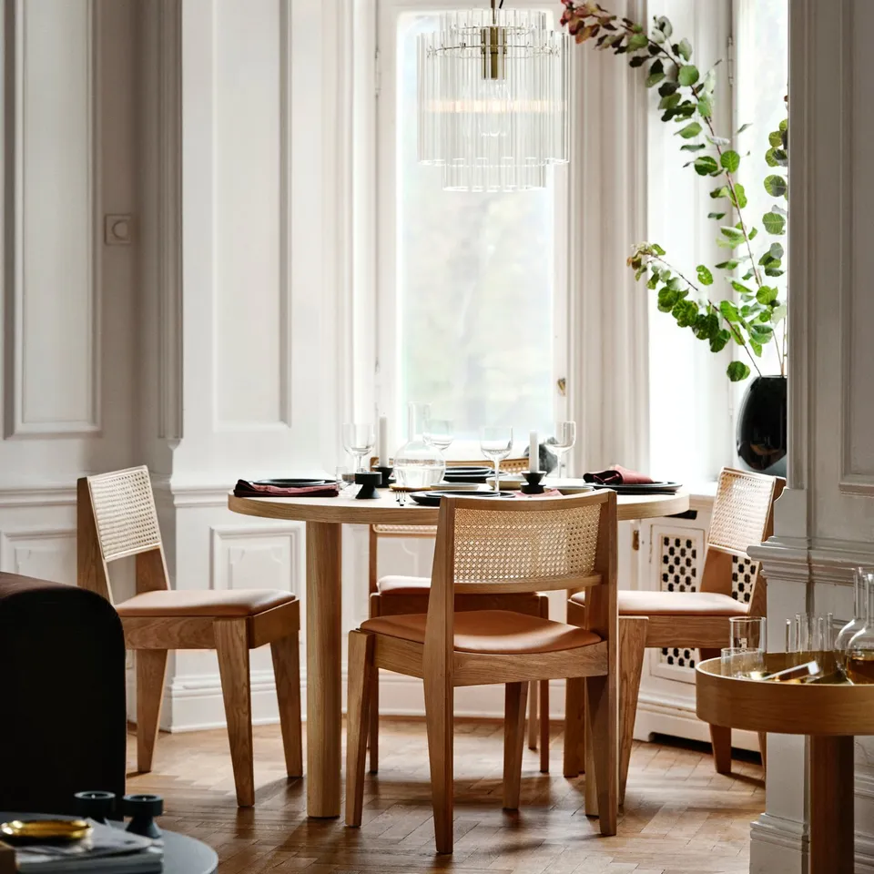 Modern dining room with wooden table, leather chairs, chandelier, and tall windows, comfortably seating small to medium groups.