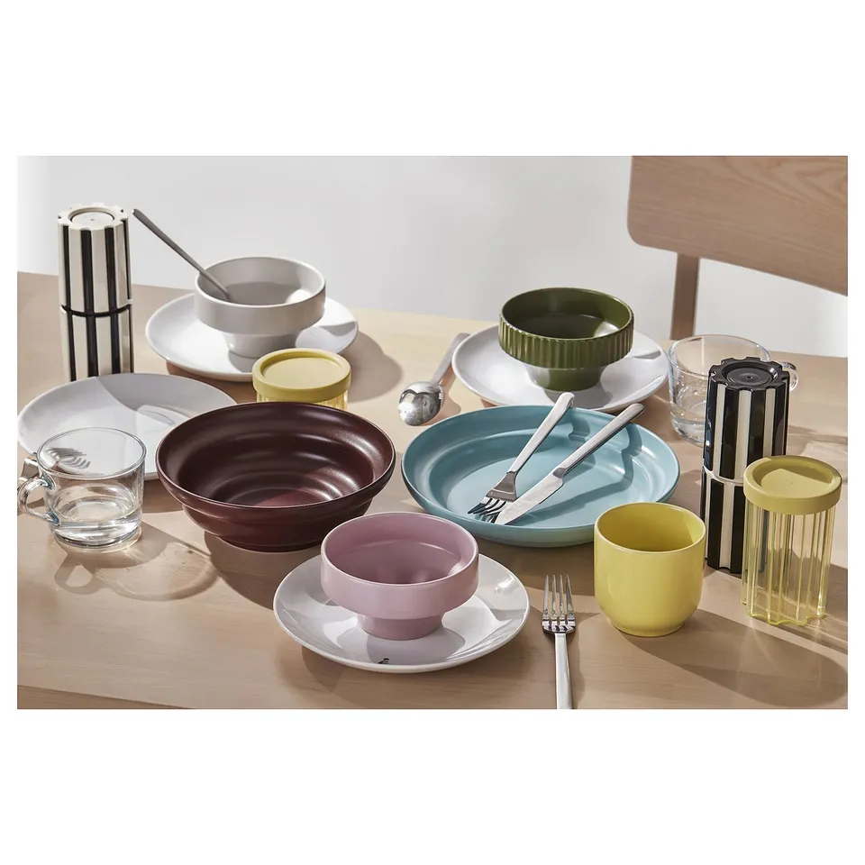 Colourful ceramic bowls and cups, black and white striped spice grinders, silverware on a wooden table.