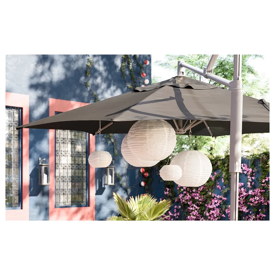 SOLVINDEN solar lamps hang from a grey patio umbrella, illuminating an outdoor space with soft light.