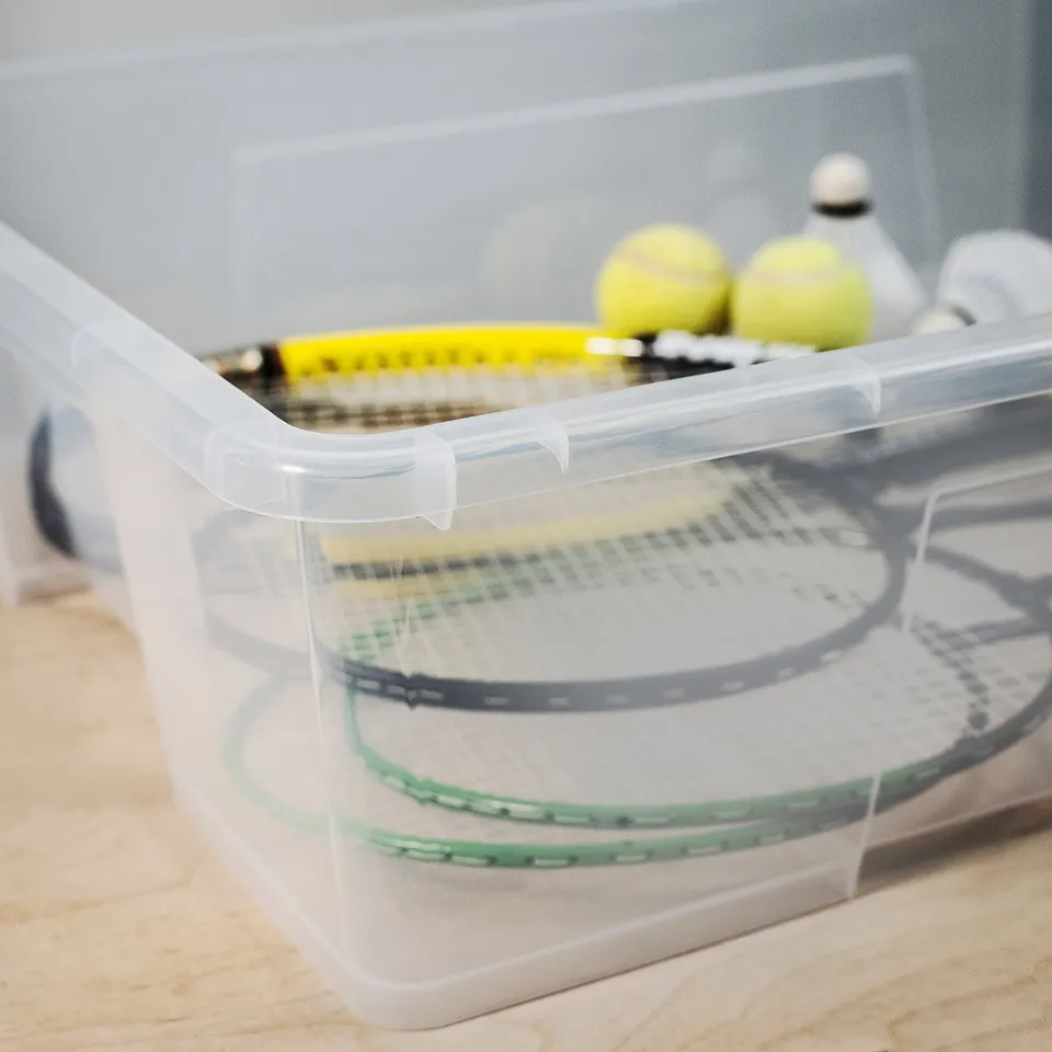 Clear plastic storage bin containing tennis rackets and balls, showcasing organised sports gear.